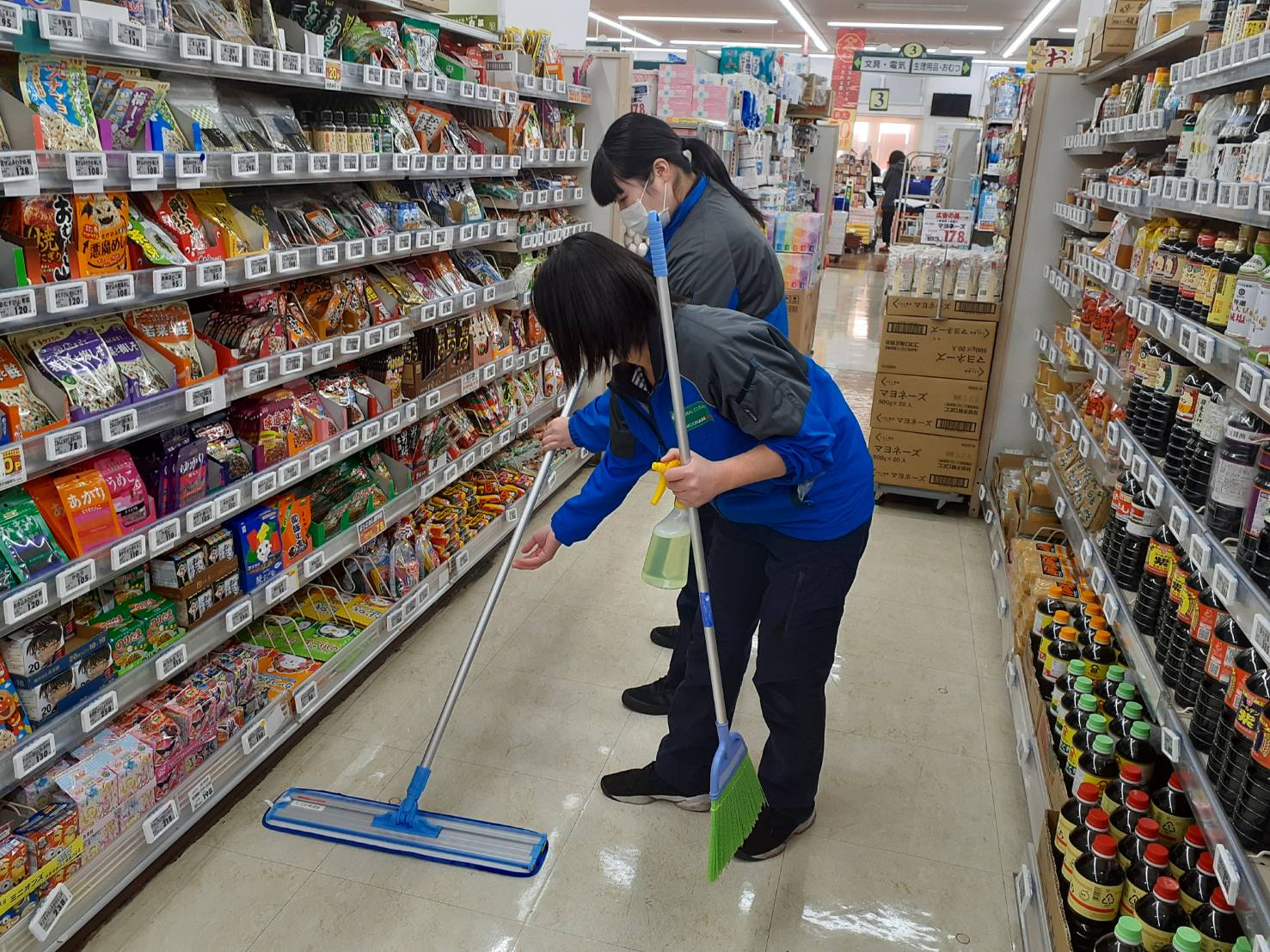 店内の通路をモップで清掃する作業着の社員